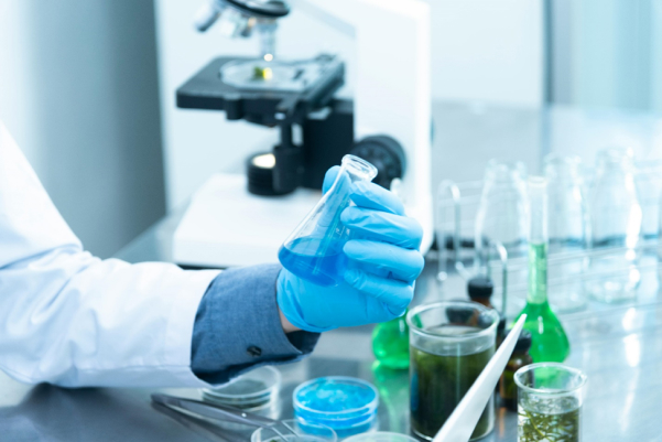 Lab technician holding a beaker with a blue substance 